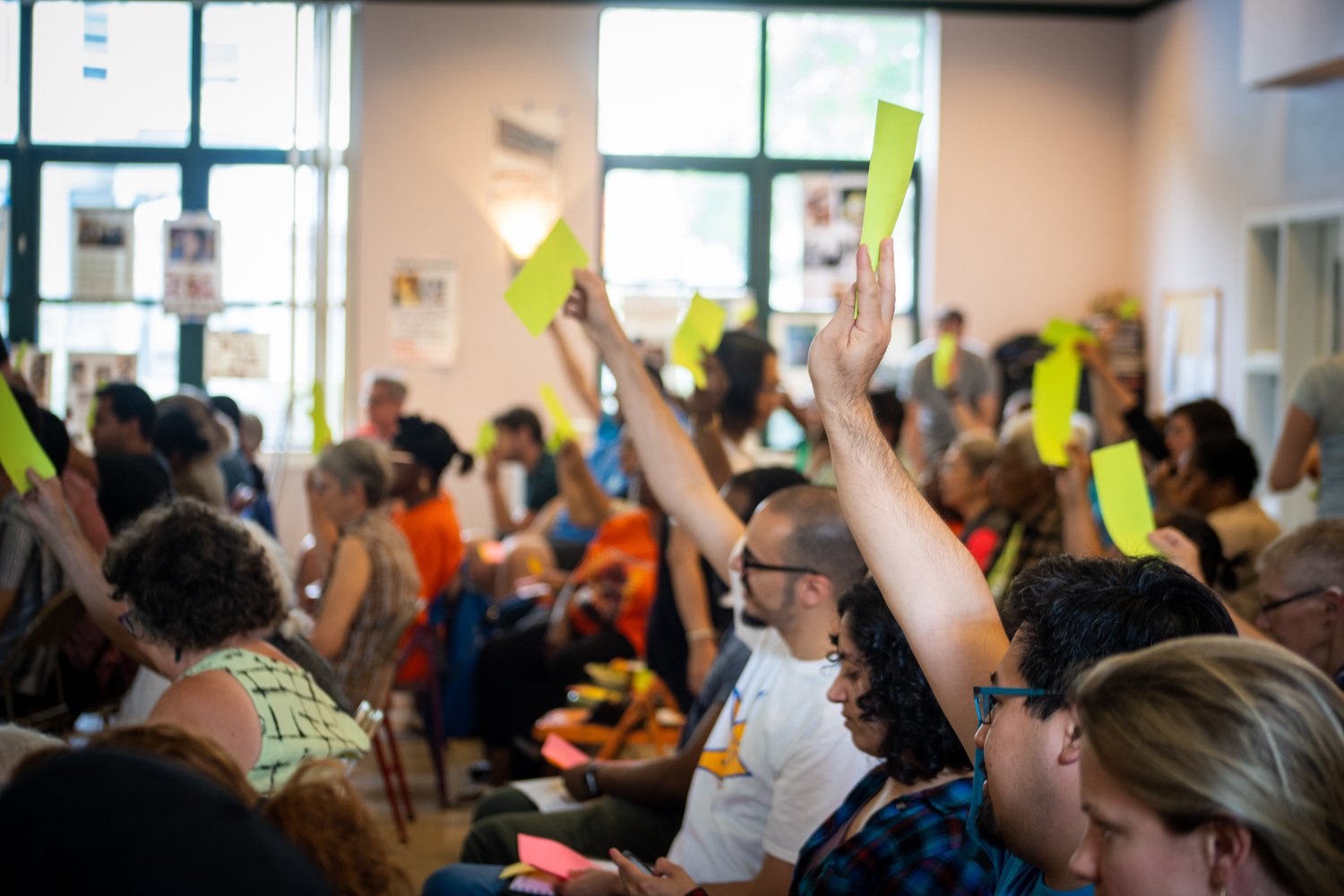 a large group of people in a big room, some holding up yellow papers to vote at the BPP Assembly in 2019
